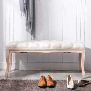 Beige tufted entryway bench with carved wood legs placed by a wall with shoes in front