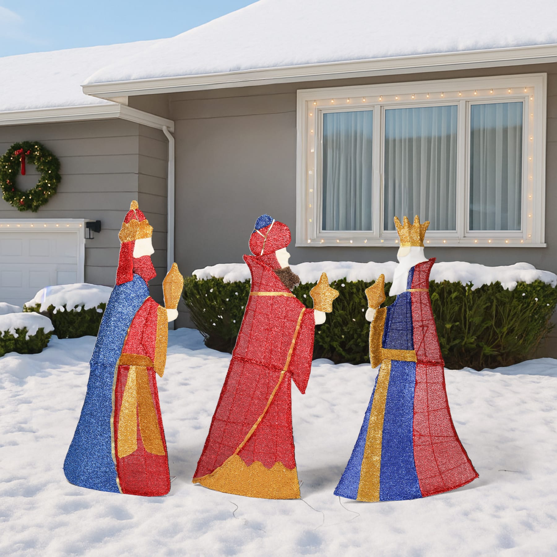 Set of three Wise Men Christmas yard decorations carrying gifts, displayed in a snowy front yard during the day